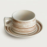 A ceramic coffee cup with a matching saucer, featuring a distressed off-white glaze with horizontal brown stripes, photographed on a clean, light off-white background.