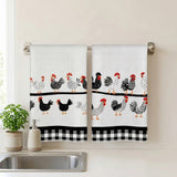Two white kitchen towels with a black and red rooster pattern hanging on a silver towel bar above a sink, with a small potted plant and soap dispenser nearby.