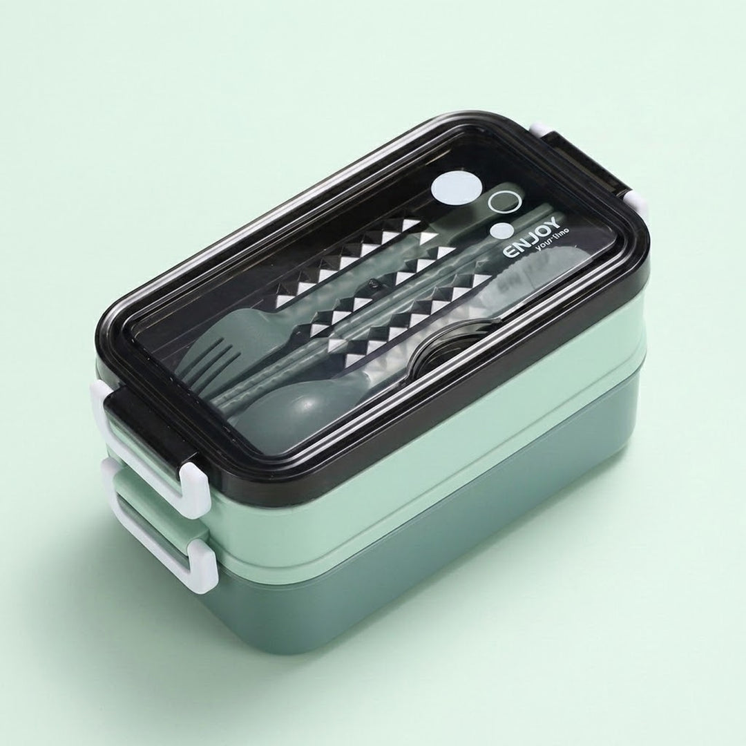 A two-tier bento lunch box with a mint green body, black lid, and white plastic handles, shown on a solid pale green background. The clear lid reveals a set of utensils inside, including a fork, spoon, and chopsticks, with the brand name 'ENJOY' printed on the lid.
