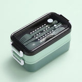 A two-tier bento lunch box with a mint green body, black lid, and white plastic handles, shown on a solid pale green background. The clear lid reveals a set of utensils inside, including a fork, spoon, and chopsticks, with the brand name 'ENJOY' printed on the lid.