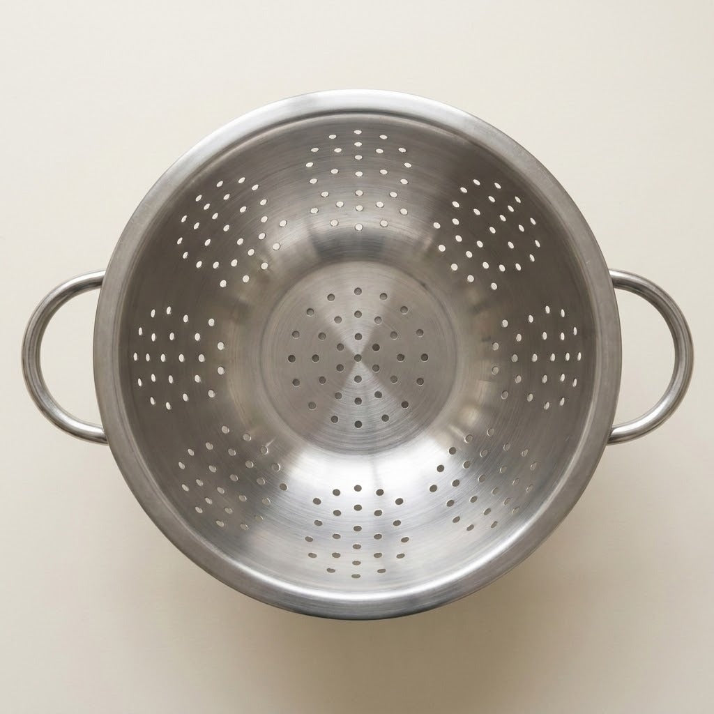 A stainless steel colander with side handles, shown from a top-down view on a light beige background.