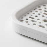 Close-up of a white plastic tray or basket with a perforated drainage design, shown on a clean white background.