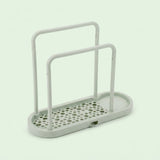 A light gray plastic organizer tray with two upright handles and a perforated base, shown on a pale mint green background.