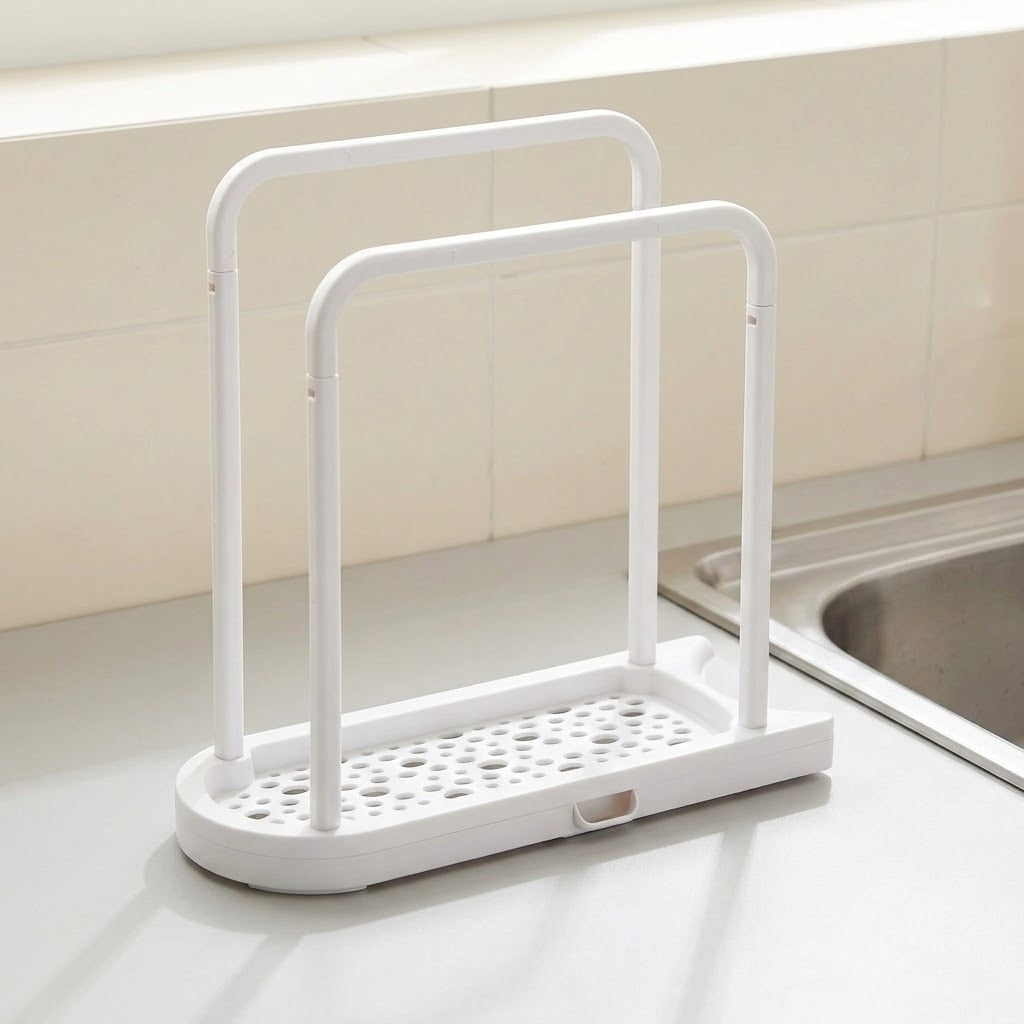 A white plastic kitchen sink organizer with two upright handles and a perforated base, placed on a light countertop next to a stainless steel sink.