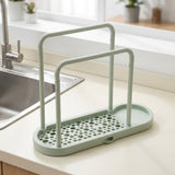 A mint green plastic kitchen sink organizer with a slotted base and two upright handles, shown on a beige countertop next to a stainless steel sink.