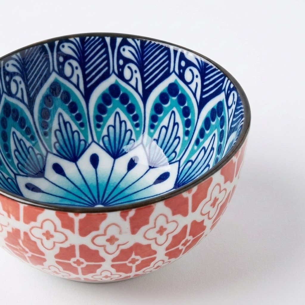 A ceramic bowl with a vibrant blue and white hand-painted mandala pattern on the inside and a coral red and white geometric pattern on the outside, shown on a clean white background.