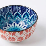 A ceramic bowl with a vibrant blue and white hand-painted mandala pattern on the inside and a coral red and white geometric pattern on the outside, shown on a clean white background.