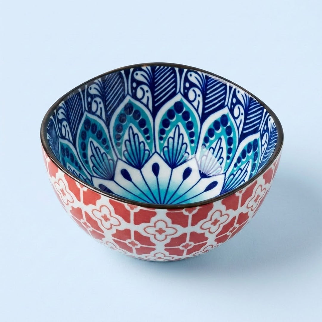 A decorative ceramic bowl with a red and white geometric pattern on the exterior and a blue and white floral mandala design on the interior, set against a light blue background.
