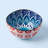 A decorative ceramic bowl with a red and white geometric pattern on the exterior and a blue and white floral mandala design on the interior, set against a light blue background.