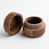 A small round wooden jar with its lid off, showing a dark interior, photographed on a clean white background.