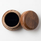 A small round wooden jar with its lid off, showing a black velvet interior, photographed on a clean white background.