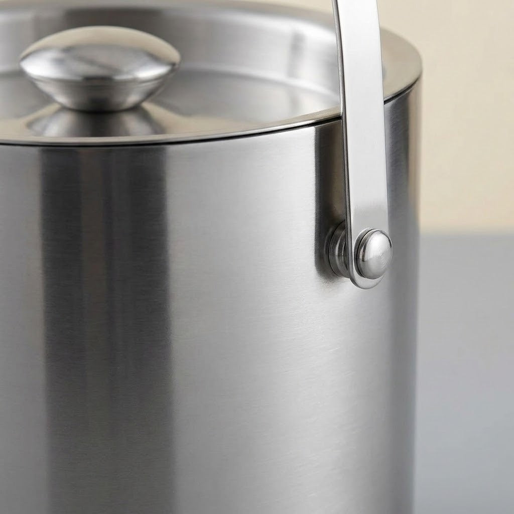 Close-up of a brushed stainless steel container with a matching lid and a vertical metal handle attached by a round rivet.