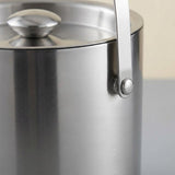 Close-up of a brushed stainless steel container with a matching lid and a vertical metal handle attached by a round rivet.