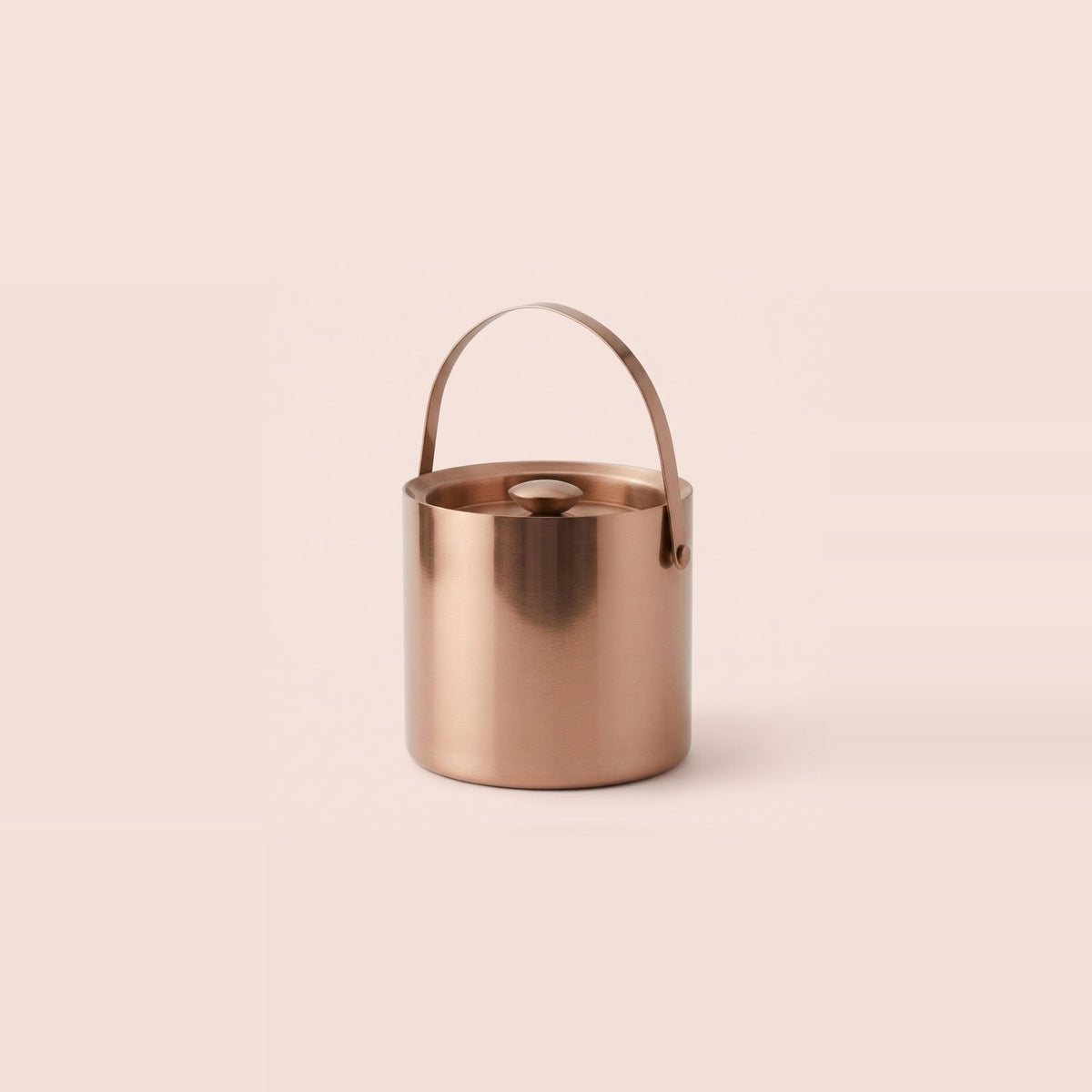 A metallic rose gold cylindrical bucket with a matching top handle, shown on a solid pale pink background.