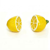 A pair of lemon-shaped stud earrings on a plain white background. One earring is shown from the side, revealing a bright yellow body with a white cross-section detail, and the other is shown from the front with a small green stem on the right.