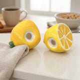 Two yellow lemon-shaped novelty items with circular cutouts, one whole and one sliced cross-section, displayed on a white countertop with a coffee mug and bowl in the background.