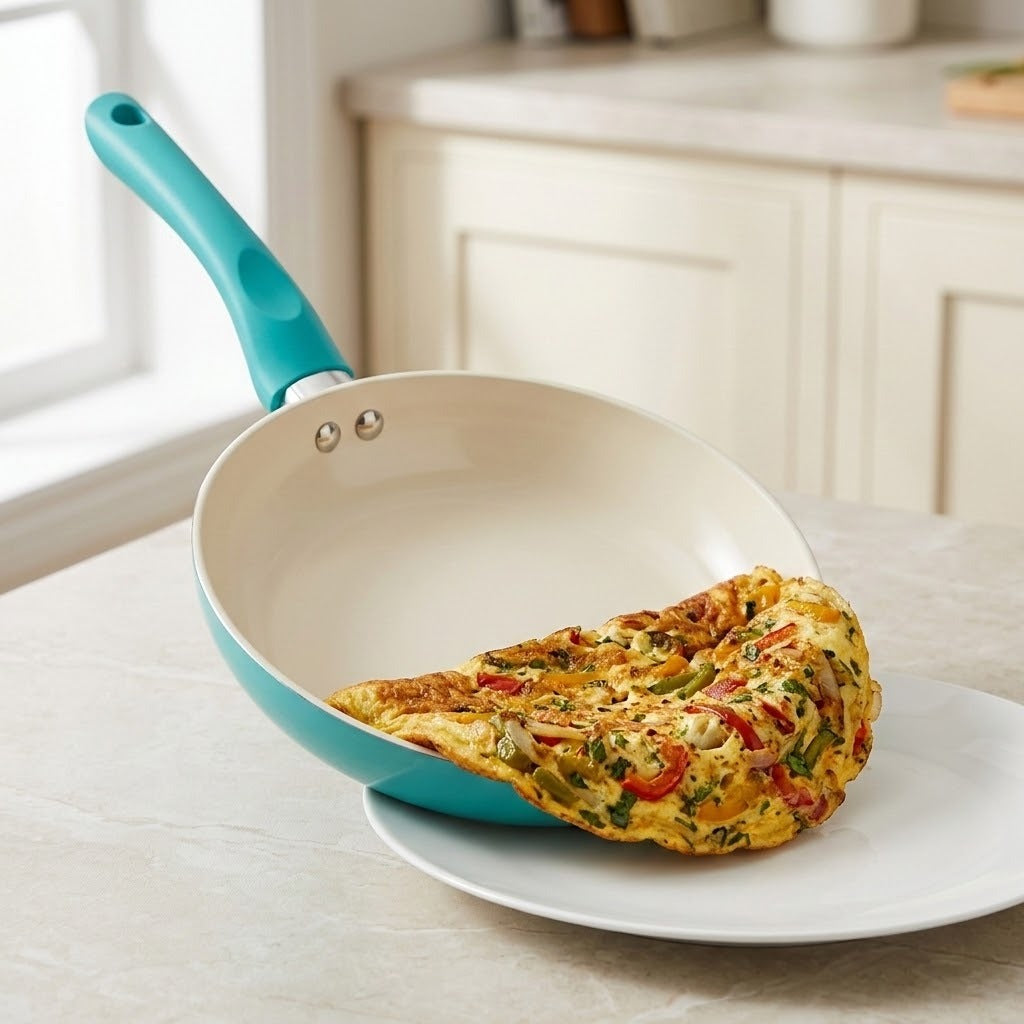 A turquoise and cream nonstick frying pan with a folded omelet resting inside, set on a white plate on a kitchen counter.