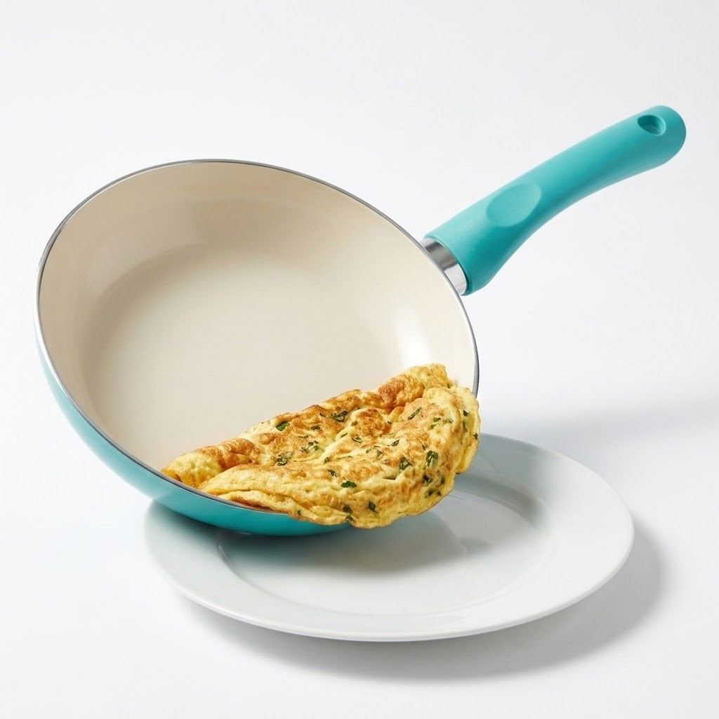 A turquoise non-stick frying pan with a cream interior, shown tilted over a white plate with a folded omelet resting inside the pan. The pan has a turquoise handle and a silver metal collar.