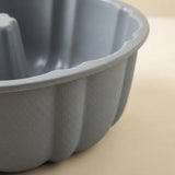 A close-up of a gray fluted bundt cake pan with a textured, pebbled exterior surface, set against a warm beige background.