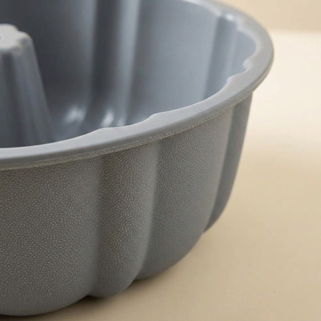 A close-up of a gray fluted bundt cake pan with a textured, pebbled exterior surface, set against a warm beige background.