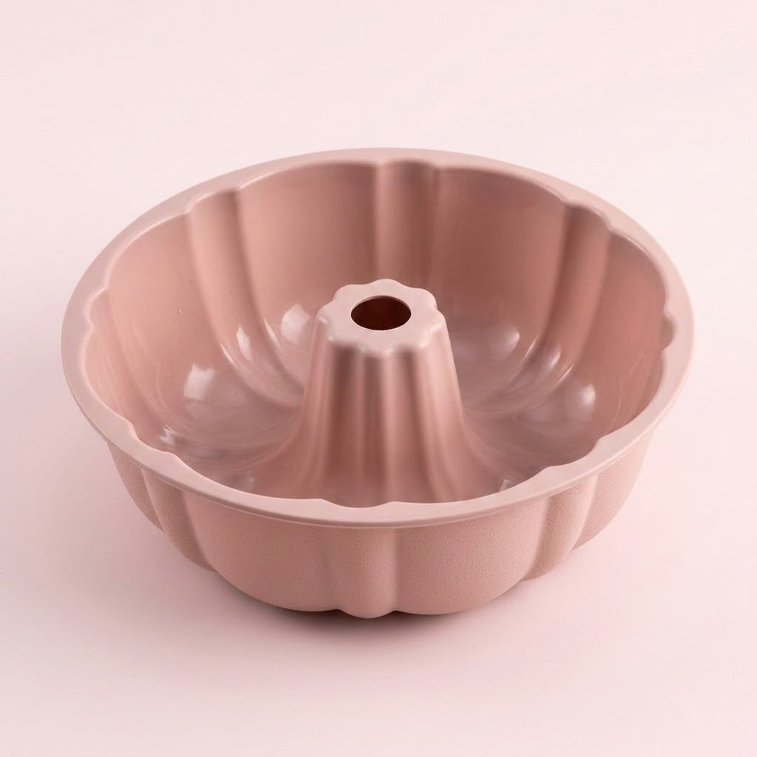 A single fluted round cake pan with a central hole, shown on a plain light pink background. The pan has a smooth matte finish and a dusty rose or mauve color.