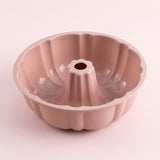 A single fluted round cake pan with a central hole, shown on a plain light pink background. The pan has a smooth matte finish and a dusty rose or mauve color.