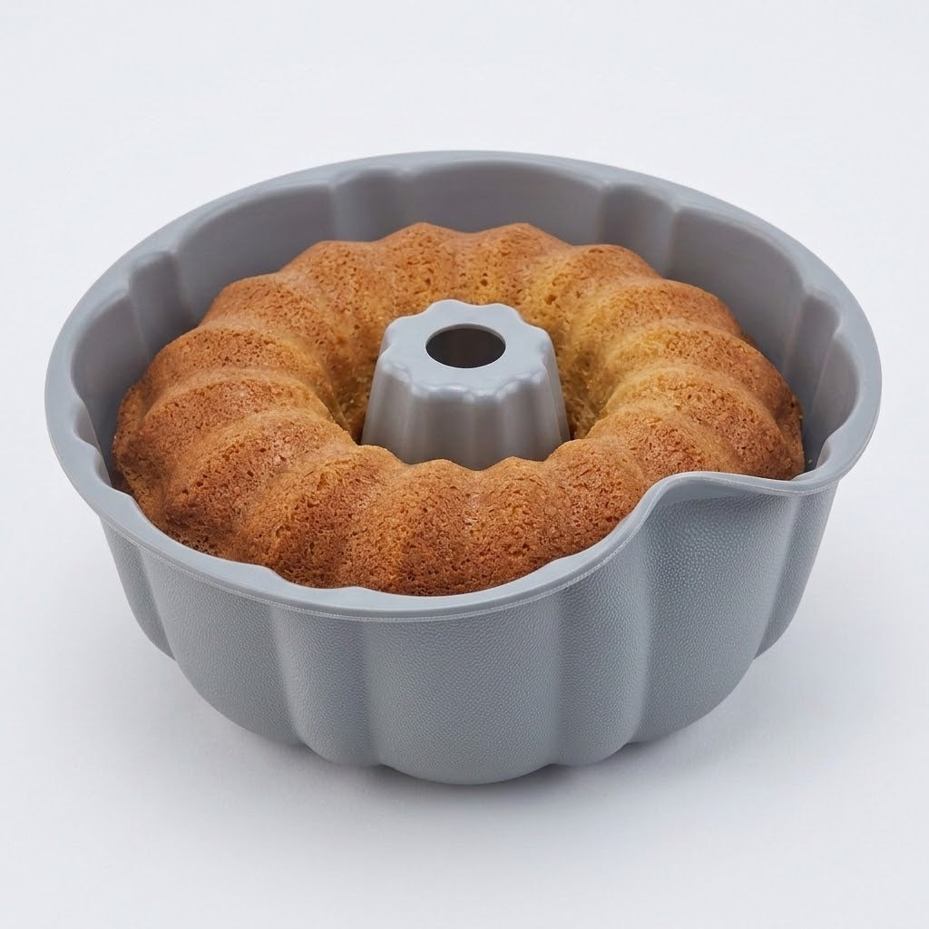 A gray fluted bundt cake pan shown with a baked golden-brown ring cake inside, photographed on a clean white background.