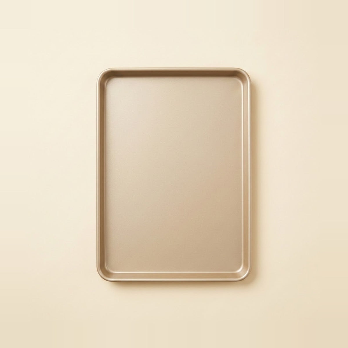 A rectangular metal baking sheet with rounded corners, shown from a top-down view on a solid, warm cream-colored background.
