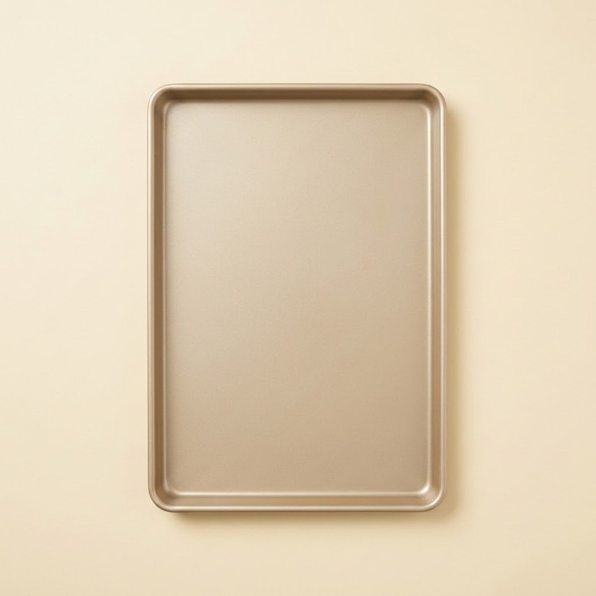 A rectangular metal baking sheet with raised edges, shown from above on a plain warm beige background.