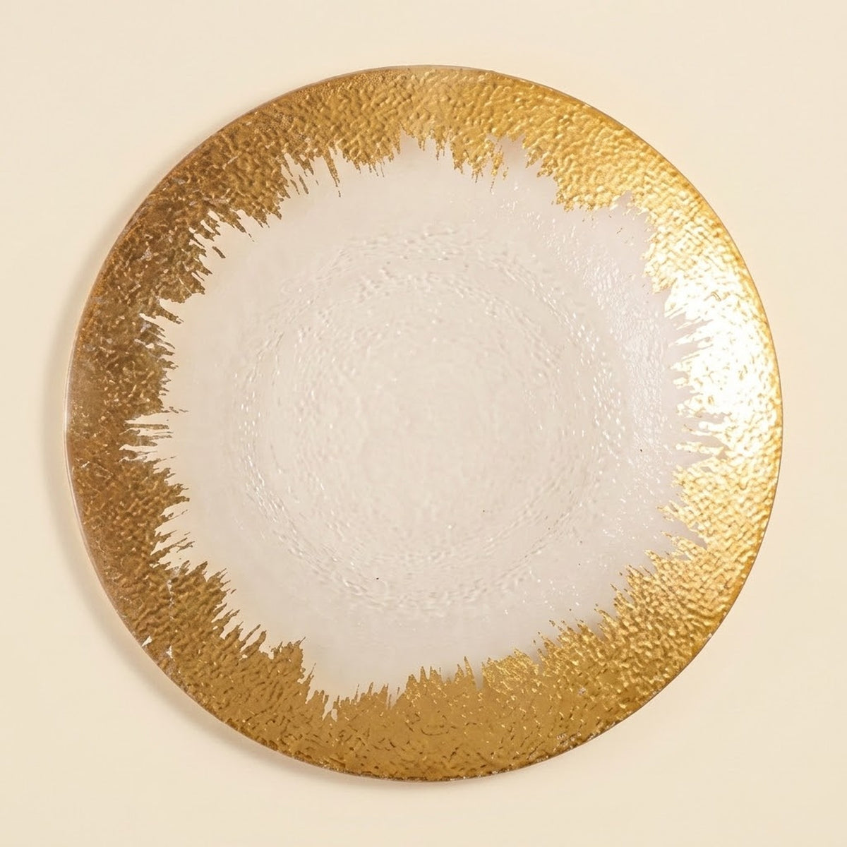 A round decorative plate with a textured metallic gold border and a smooth white center, photographed from directly above on a light cream background.