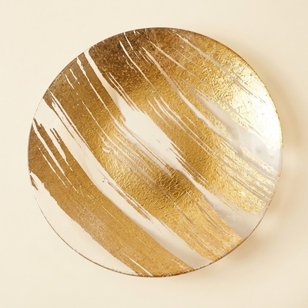 A round decorative plate featuring a textured gold and white abstract brushstroke pattern, photographed from directly above on a light beige background.