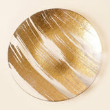 A round decorative wall art piece featuring a gold and white abstract brushstroke pattern, shown against a solid cream background.