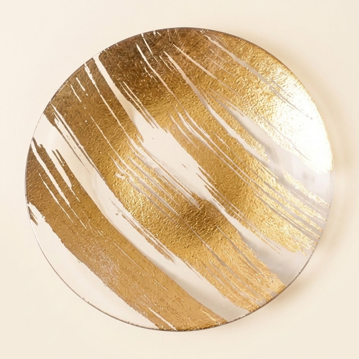 A round decorative wall art piece featuring a gold and white abstract brushstroke pattern, shown against a solid cream background.