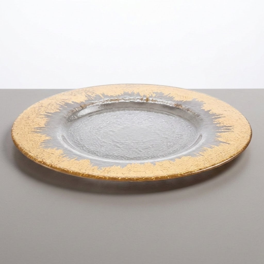 A round glass charger plate with a textured clear center and a wide gold-rimmed border, shown on a neutral gray surface against a white background.