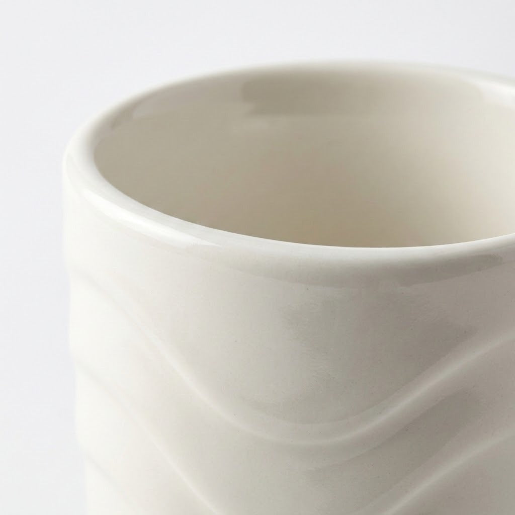 Close-up of a glossy ceramic mug with a wavy, ribbed exterior pattern in a warm off-white or cream color, set against a plain white background.