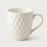A white ceramic coffee mug with a textured honeycomb pattern and a curved handle, shown on a light gray background.