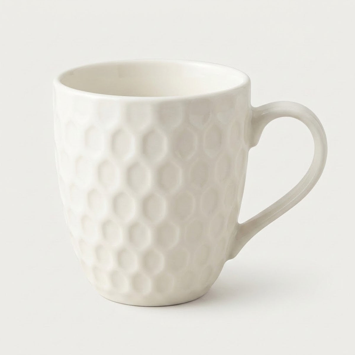 A white ceramic coffee mug with a textured honeycomb pattern and a curved handle, shown on a light gray background.