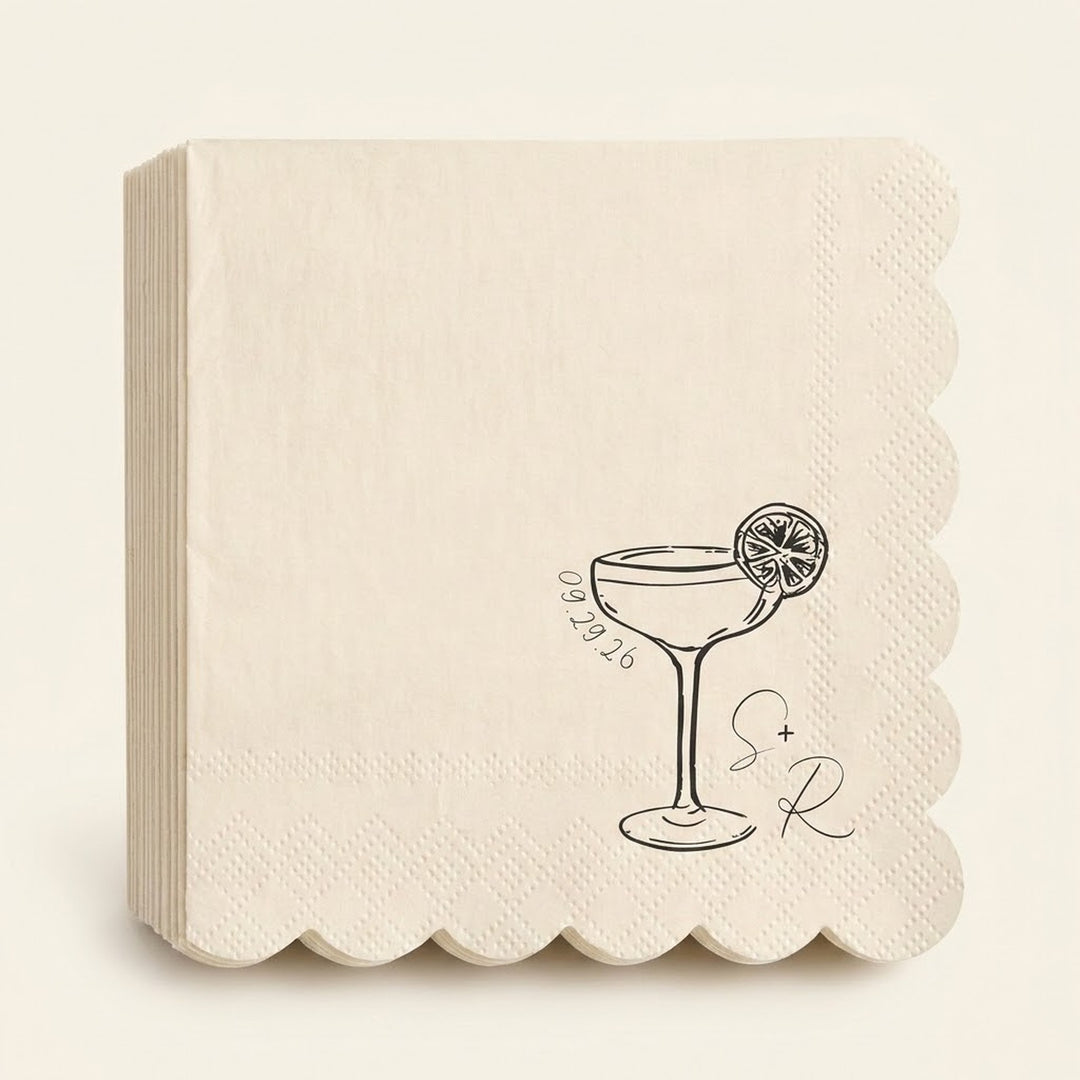 A stack of cream-colored paper napkins with scalloped edges, featuring a black line art illustration of a martini glass with a lemon slice, the date '09.29.