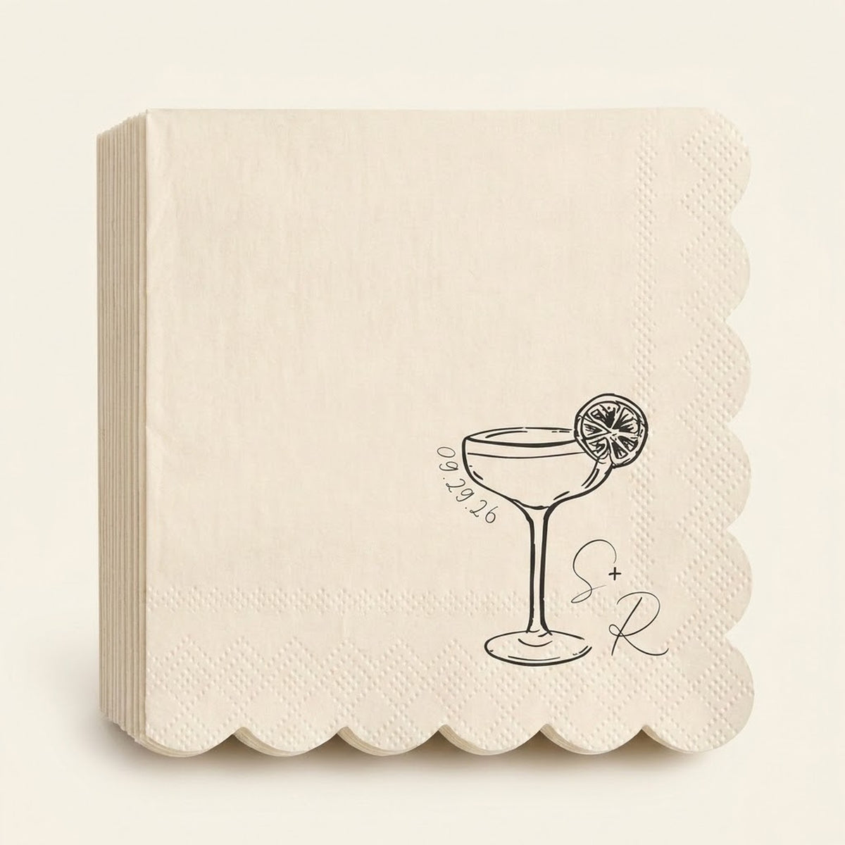 A stack of cream-colored paper napkins with scalloped edges, featuring a black line art illustration of a martini glass with a lemon slice, the date '09.29.