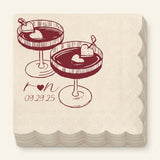 A stack of square paper napkins with scalloped edges, printed with two cocktail illustrations and the text 'ron 09.29.