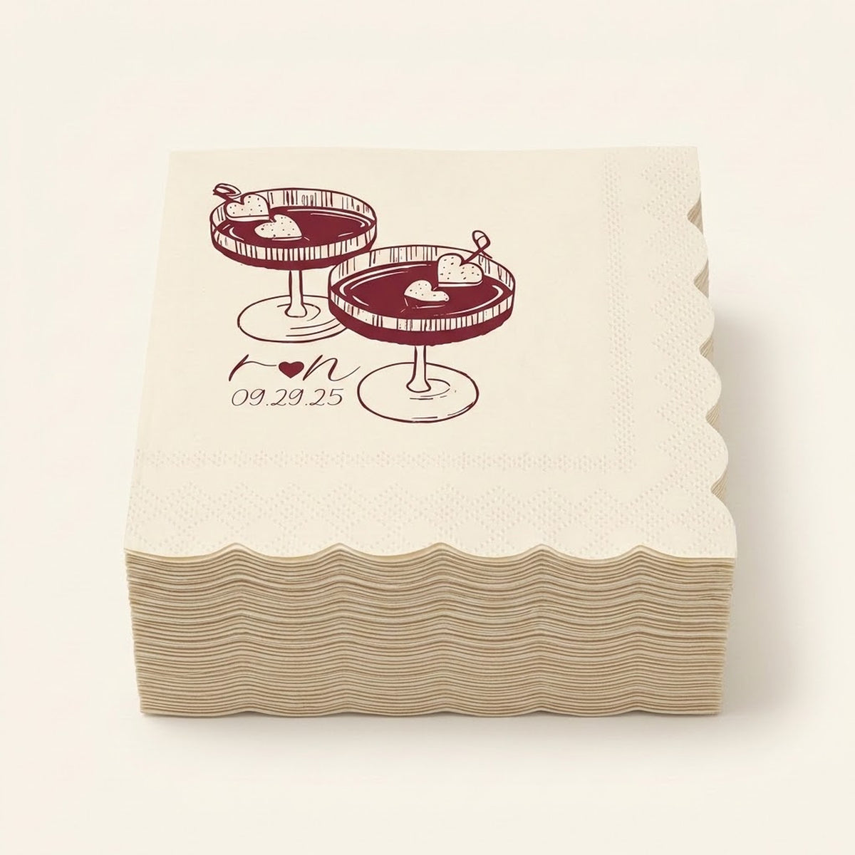 A stack of square paper napkins with scalloped edges, printed with an illustration of two dessert cocktails and the date '09.29.