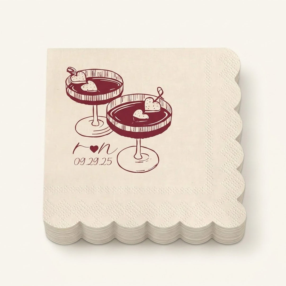 A stack of square cream paper napkins with scalloped edges, printed with a dark red illustration of two cocktails and the date '09.29.