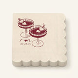 A stack of square cream paper napkins with scalloped edges, printed with a dark red illustration of two cocktails and the date '09.29.