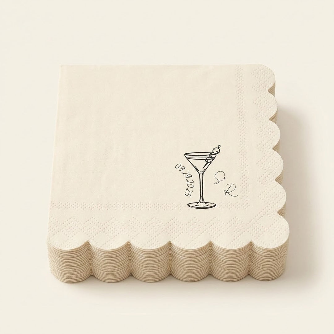 A stack of square off-white paper napkins with scalloped edges, featuring a black line art illustration of a martini glass with an olive and the words 'Groomsmen' alongside a monogram.