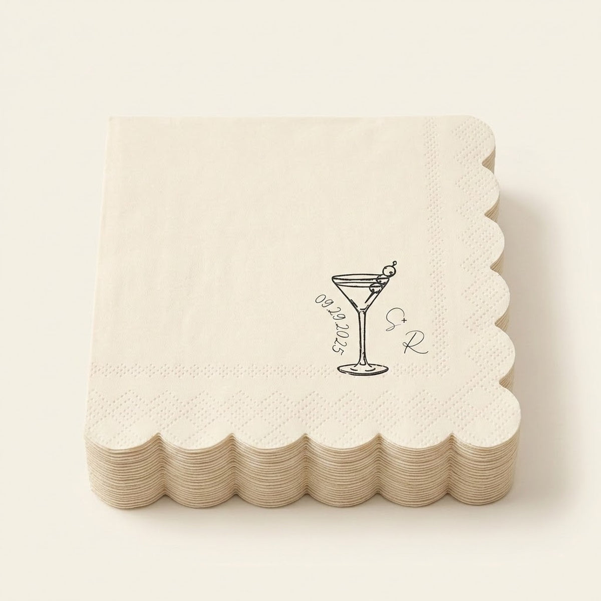 A stack of square off-white paper napkins with scalloped edges, featuring a black line art illustration of a martini glass with an olive and the words 'Groomsmen' alongside a monogram.