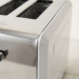 Close-up of a stainless steel and white toaster, showing the side panel, brushed metal edge, and part of the top slot opening.