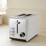 A modern two-slice toaster with a brushed silver metallic finish and black accents, shown on a light beige countertop in a kitchen setting.