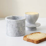 A marble egg cup and matching marble egg stand on a white surface, with a slice of toast spread with butter in the foreground.