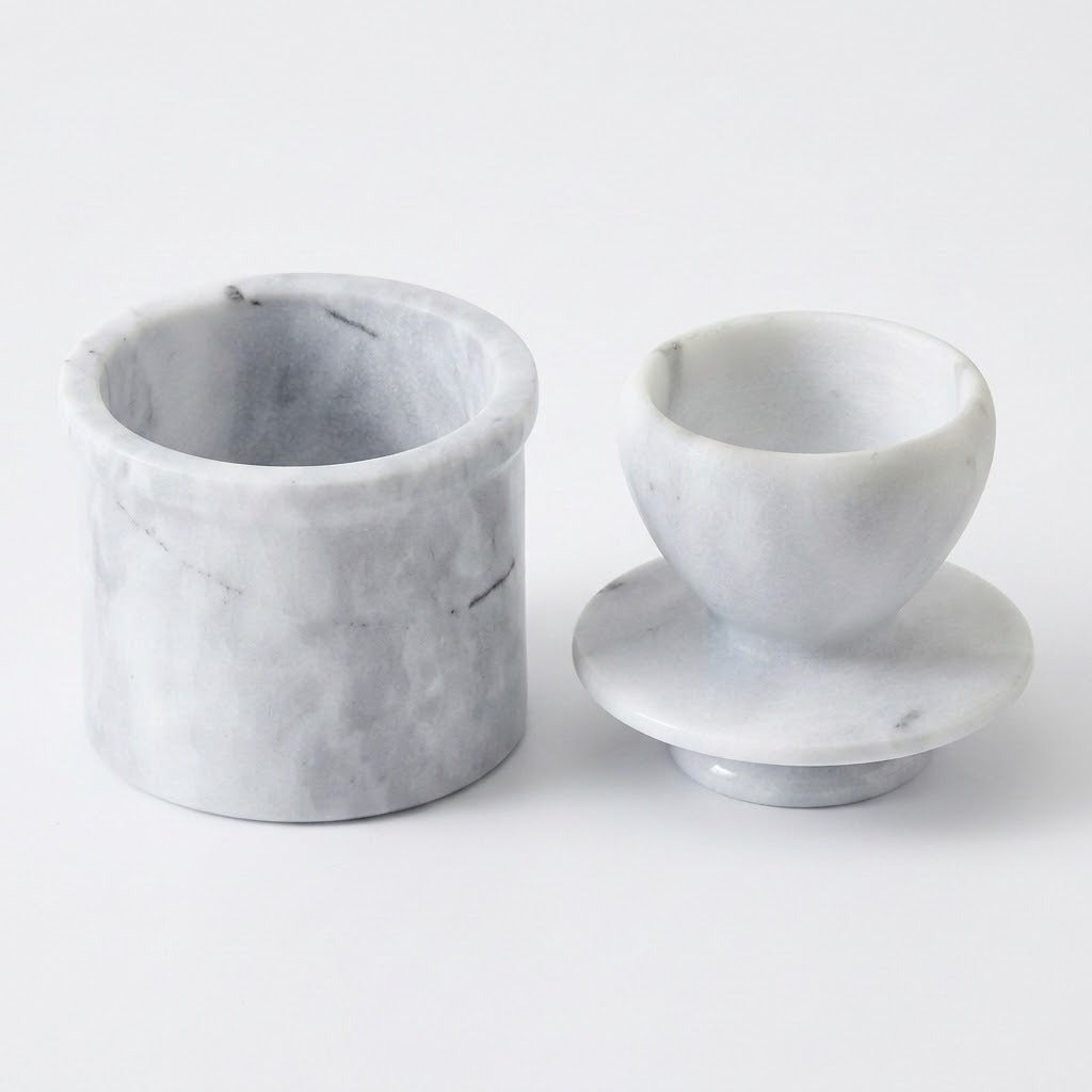 A pair of small round marble containers or cups, one cylindrical and one rounded with a matching base, shown on a clean white background.