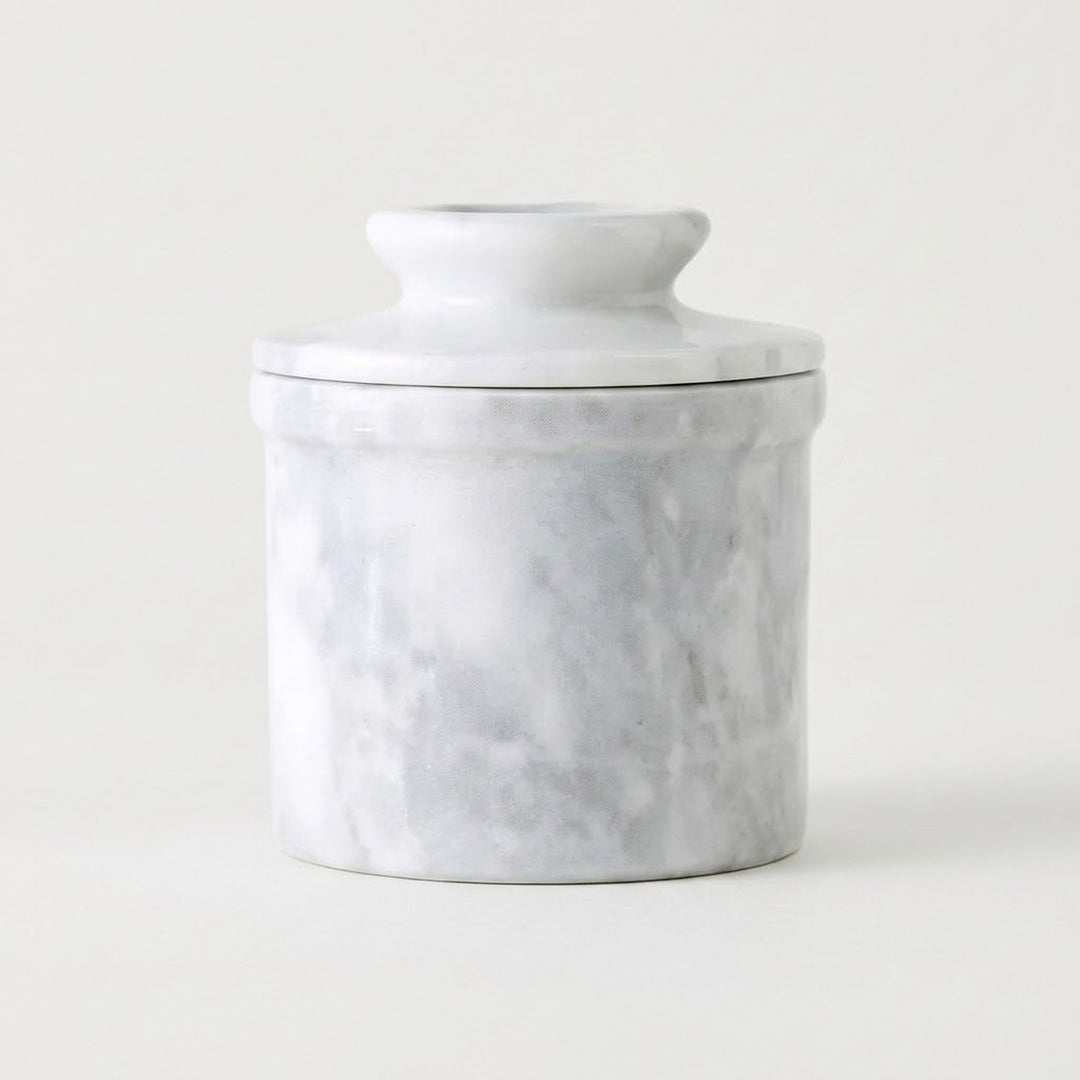 A small cylindrical lidded jar or container with a white marble-look surface and soft gray veining, photographed on a clean white background.